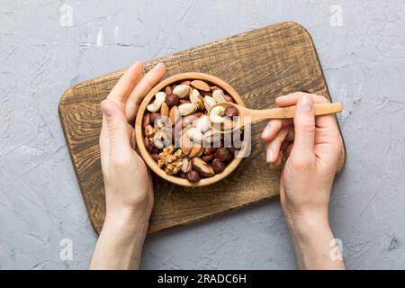 Frauenhände halten eine Holzschüssel mit gemischten Nüssen, Walnuss, Pistazien, Mandeln, Haselnüssen und Cashews. Gesundes Essen und Snack. Vegetarische Snacks dif Stockfoto