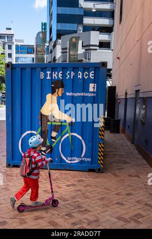 Ein kleines Kind auf einem Mini-Roller passiert ein Wandbild eines Fahrrads auf einem Schiffscontainer in der Hafengegend Wellington, Hauptstadt Neuseelands Stockfoto