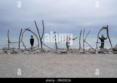 Die Menschen stehen auf dem Treibholz-Strandschild für die Küstenstadt Hokitika am State Highwway 6 an der Westküste von South Island, Neuseeland Stockfoto