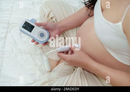 Nahaufnahme einer jungen schwangeren Frau mit einem fetalen Droppler, um den Herzschlag des Babys zu hören Stockfoto