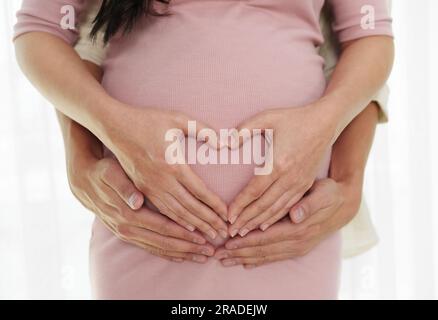 Nahaufnahme eines schwangeren Paares, das eine Hand-Herz-Geste auf dem Bauch macht Stockfoto