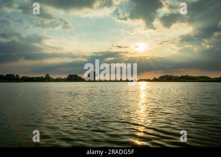 Die untergehende Sonne in den Wolken über dem See, Sommerblick Stockfoto