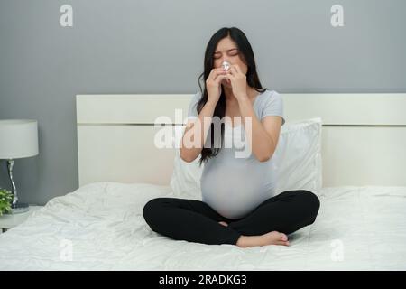 Schwangere Frau, verstopfte Nase, Niesen, Halsschmerzen auf einem Bett. Grippe in der Schwangerschaft Stockfoto