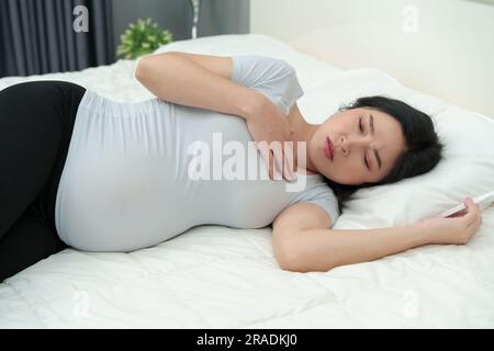 Schwangere Frau fühlt sich schlecht auf einem Bett Stockfoto