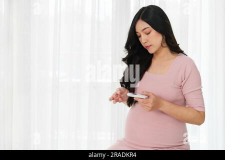 Junge Schwangere, die ein Blutzuckermessgerät in der Hand hält und zu Hause den Blutzuckerspiegel kontrolliert. Gestationsdiabetes-Konzept. Stockfoto