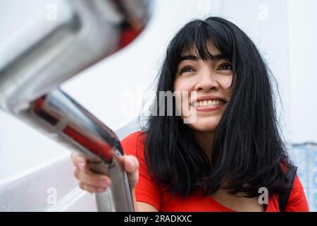 Nahaufnahme einer wunderschönen jungen lateinischen Frau venezolanischer Herkunft, in Rot mit schwarzem Haar, draußen, die aufmerksam, lächelnd und neugierig aussieht, Leute CO Stockfoto