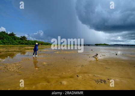 Frau, die mit einem Hund am Ufer von Lough Cullin, Pontoon, County Mayo, Irland, spaziert, mit Sturmwolken darüber Stockfoto