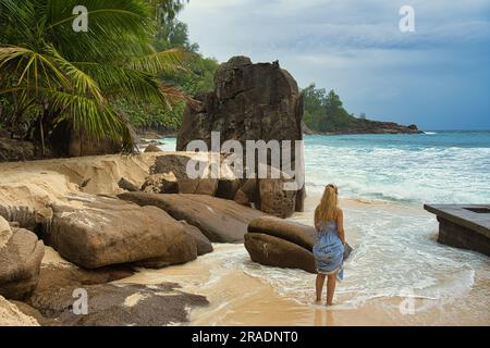 Wunderschöne Felsbrocken und weißer Sandstrand von intendance, eine Frau mittleren Alters, die zwischen Felsen und Wellen steht, Mahe Seychellen Stockfoto