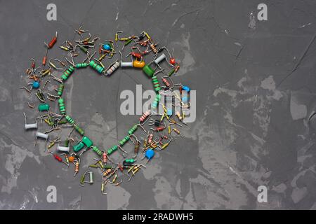 Herzform aus elektronischen Bauteilen auf grauem Betonhintergrund. Symbol der Liebe von Widerständen und Kondensatoren. Happy Valentines Day Gruß c Stockfoto