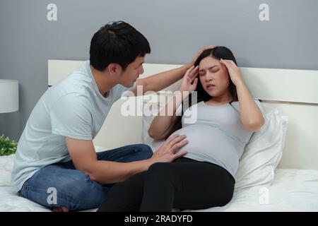 Schwangere Frau hat Kopfschmerzen mit ihrem Mann auf dem Bett Stockfoto