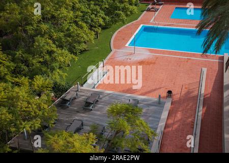 Entspannen Sie sich in einer sonnigen Oase im Freien: Sonnenliegen, Swimmingpool und Dusche im Freien in einem ruhigen Hotelgarten Stockfoto