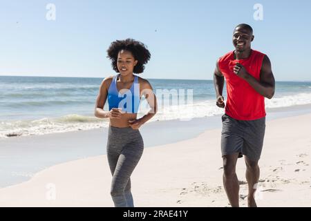 Glückliches, fittes afroamerikanisches Paar, das am sonnigen Strand trainiert Stockfoto