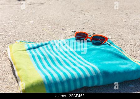 Rote Sonnenbrille auf grün-blau gestreiftem Handtuch am sonnigen Sandstrand, Kopierbereich Stockfoto