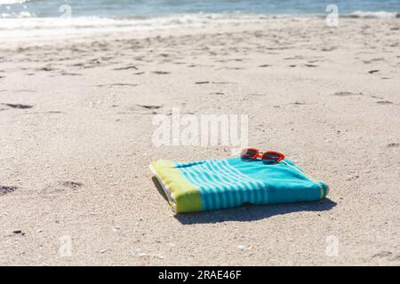 Rote Sonnenbrille auf grün-blau gestreiftem Handtuch am sonnigen Sandstrand am Meer, Kopierbereich Stockfoto