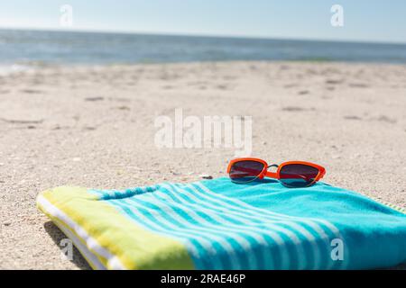 Rote Sonnenbrille auf grün-blau gestreiftem Handtuch am sonnigen Sandstrand am Meer, Kopierbereich Stockfoto