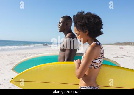 Fit afroamerikanisches Paar mit Surfbrettern am sonnigen Strand am Meer Stockfoto