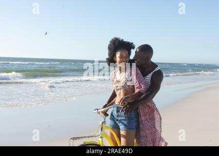 Glückliches afroamerikanisches Paar, das Spaß beim Fahrradfahren am sonnigen Strand auf dem Meer hat Stockfoto