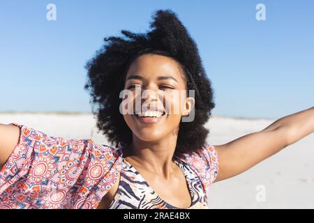 Eine glückliche afroamerikanische Frau lächelt am sonnigen Strand mit ausgestreckten Armen Stockfoto