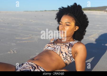 Glückliche afroamerikanische Frau im Bikini, die am sonnigen Strand liegt Stockfoto