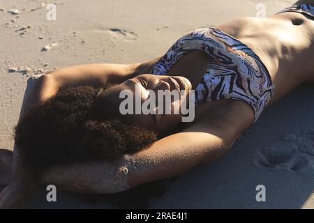 Glückliche afroamerikanische Frau im Bikini, die sich am sonnigen Strand sonnt Stockfoto