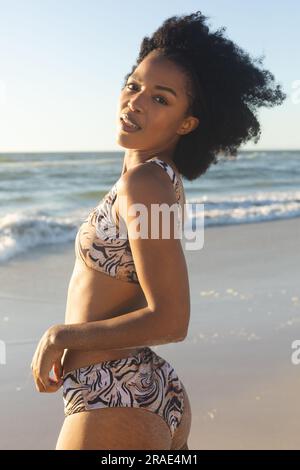 Porträt einer glücklichen afroamerikanischen Frau im Bikini, die am sonnigen Strand am Meer lächelt Stockfoto