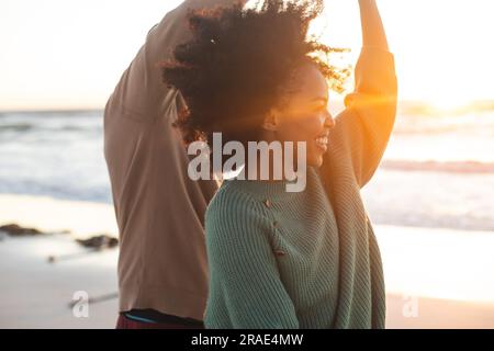 Glückliches afroamerikanisches Paar, das am sonnigen Strand tanzt und lächelt Stockfoto