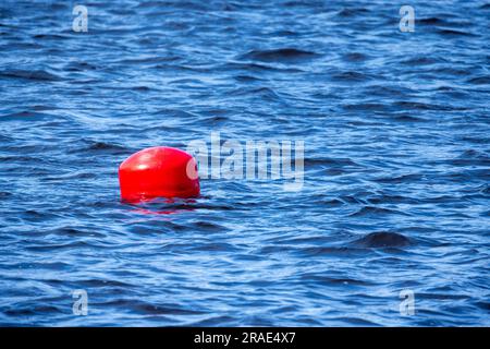 Rote kugelförmige Boje, die an einem sonnigen Tag auf blauem Meerwasser schwimmt Stockfoto
