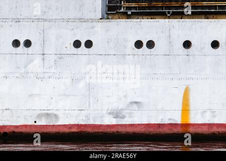 Alter Schiffskörper mit roter Wasserlinie und Bullaugen, Hintergrund-Fotostruktur für den industriellen Transport Stockfoto