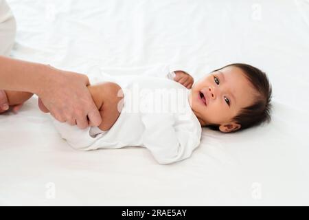 Mutterhände halten Babybeine und machen spielerische Übungen auf dem Bett Stockfoto