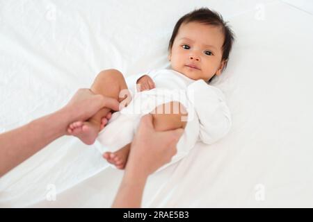 Mutterhände halten Babybeine und machen spielerische Übungen auf dem Bett Stockfoto