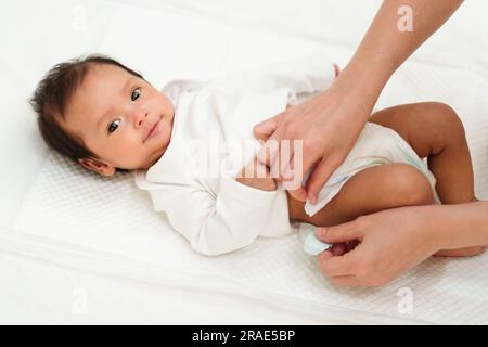 Mutter, die die Windel des Neugeborenen wechselt, während sie auf dem Bett liegt Stockfoto