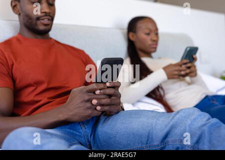 afroamerikanisches Paar, das Smartphones benutzt und im Schlafzimmer auf dem Bett liegt Stockfoto