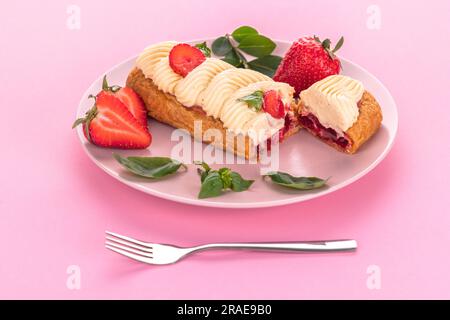 französischer eclair mit Schokolade und fruchtiger Erdbeercreme oder süßen italienischen Profiterolen und frischen, saftigen Erdbeeren, Essen auf rosa Hintergrund Stockfoto