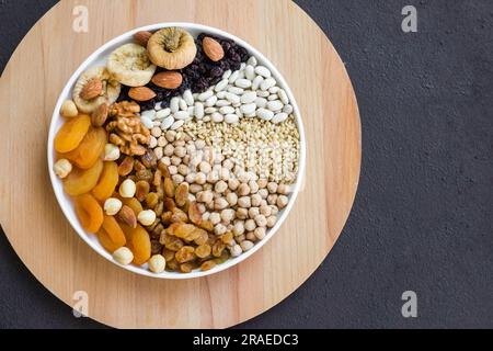 Ungekochte Ashura-Zutaten Kichererbsen, Weizen, Reis und weiße Bohnen, Nüsse und süße Früchte, die auf einer weißen Platte auf dunkler Oberfläche mit Kopierbereich entworfen wurden Stockfoto