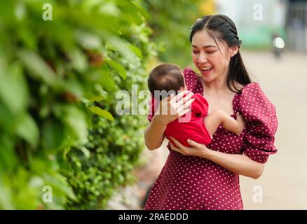 Mutter hält und spielt mit ihrem Neugeborenen im Garten Stockfoto