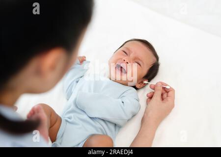 Mutter, die Wattestäbchen benutzt, um das Ohr eines weinenden Neugeborenen auf einem Bett zu putzen Stockfoto