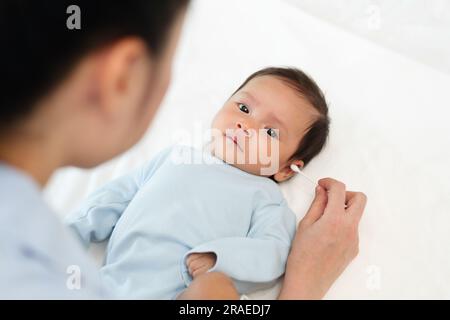 Mutter, die Wattestäbchen benutzt, um das Ohr des Neugeborenen auf einem Bett zu putzen Stockfoto