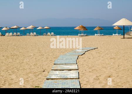 Wanderweg am heißen Sand am Strand mit verschwommenen Korbschirmen und Sonnenliegen Stockfoto