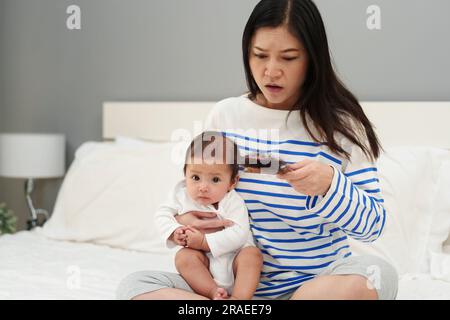 Gestresste Mutter mit Haarausfall nach der Geburt mit ihrem Baby zu Hause Stockfoto