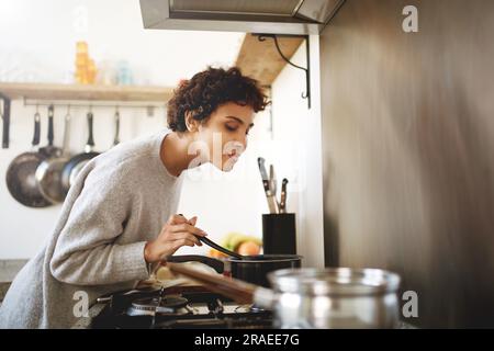 Porträt einer jungen Frau, die Essen aus dem Topf kocht und riecht Stockfoto