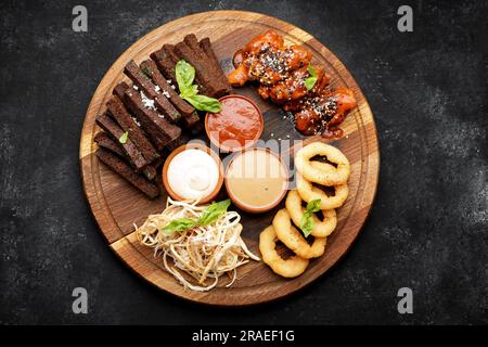 Eine Auswahl an Biervorspeisen mit verschiedenen Saucen auf einem Holzbrett. Calamari, Grillflügel, Knoblauch-Croutons Stockfoto