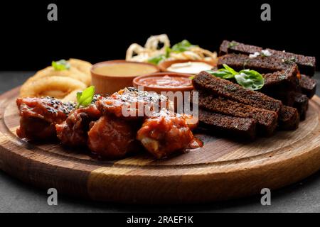 Eine Auswahl an Biervorspeisen mit verschiedenen Saucen auf einem Holzbrett. Calamari, Grillflügel, Knoblauch-Croutons Stockfoto