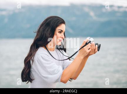 Junge, schöne Frau, die draußen Fotos mit einer alten Filmkamera macht Stockfoto