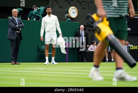 Novak Djokovic inspiziert die Feuchtigkeit auf dem Platz und beobachtet das Bodenpersonal, das Laubblasgeräte herausbringt, um während einer Verzögerung des Spiels bei Regen am ersten Tag der Wimbledon Championships 2023 im All England Lawn Tennis and Croquet Club in Wimbledon das Gras zu trocknen. Foto: Montag, 3. Juli 2023. Stockfoto