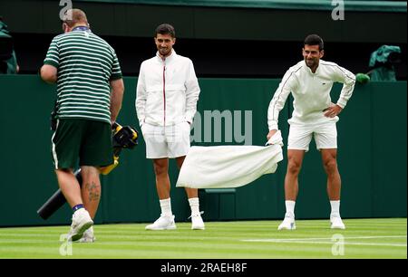 Novak Djokovic inspiziert die Feuchtigkeit auf dem Platz und beobachtet das Bodenpersonal, das Laubblasgeräte herausbringt, um während einer Verzögerung des Spiels bei Regen am ersten Tag der Wimbledon Championships 2023 im All England Lawn Tennis and Croquet Club in Wimbledon das Gras zu trocknen. Foto: Montag, 3. Juli 2023. Stockfoto