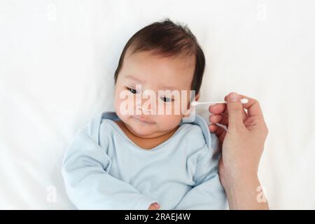 Mutter, die Wattestäbchen benutzt, um das Ohr des Neugeborenen auf einem Bett zu putzen Stockfoto