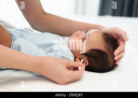 Mutter, die Wattestäbchen benutzt, um das Ohr des Neugeborenen auf einem Bett zu putzen Stockfoto