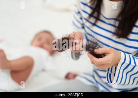 Gestresste Mutter mit Haarausfall nach der Geburt mit ihrem Baby zu Hause Stockfoto