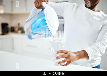 Person, Kanne und ein Glas Filterwasser in der Küche für frisches Getränk, Flüssigkeit und Hydratation. Nahaufnahme, durstige Frau oder reines Wassergetränk einschenken Stockfoto