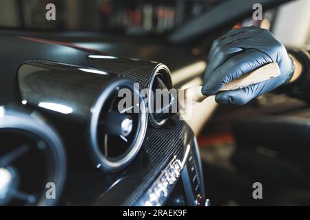 Autobelüftung wird mit professioneller Auto-Detailbürste gereinigt. Ein unbekannter Tiefreinigungsexperte in schwarzem Schutzhandschuh. Hochwertiges Foto Stockfoto